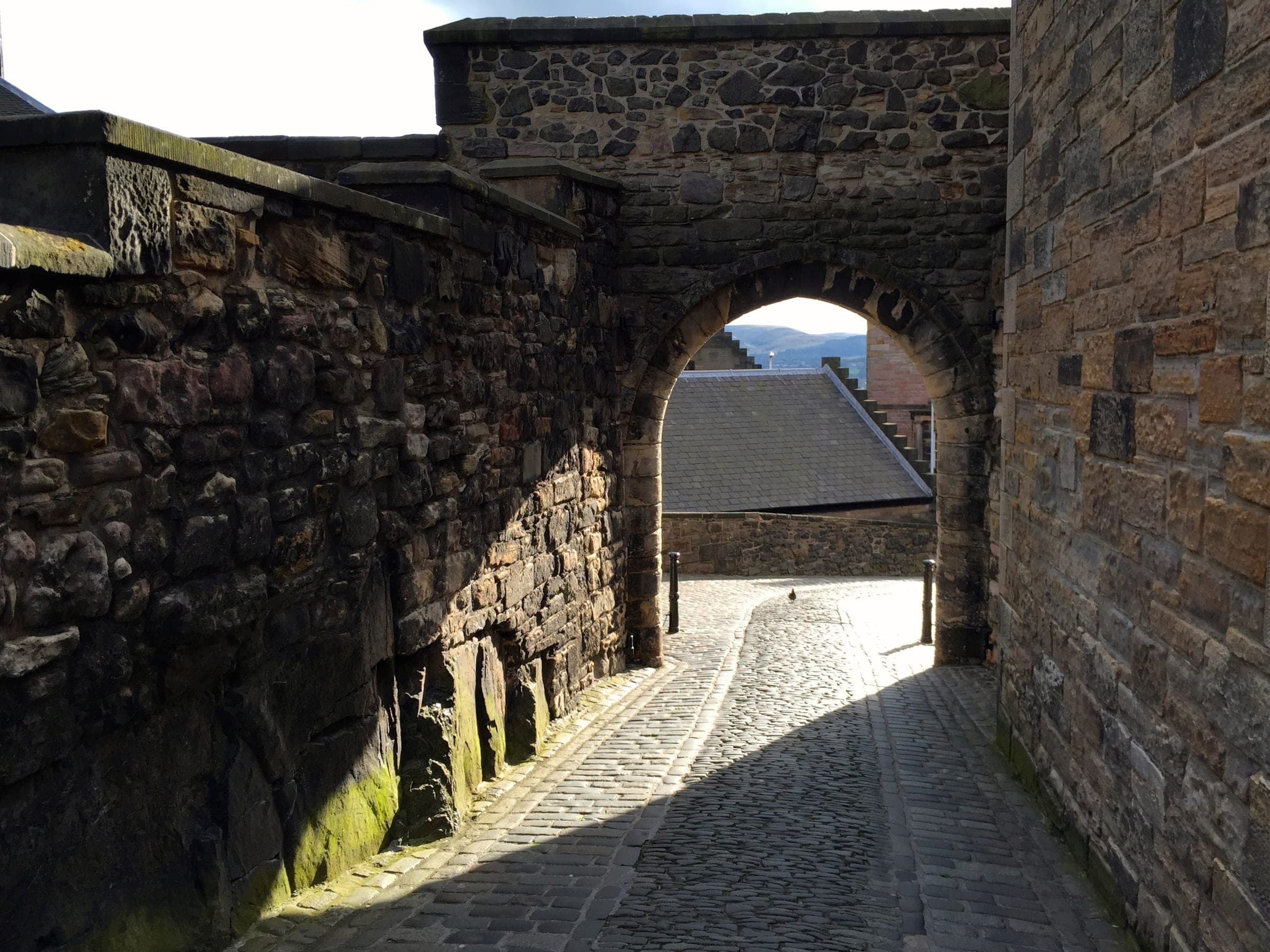A cobbled lane between old stone walls, running through an arched gateway.