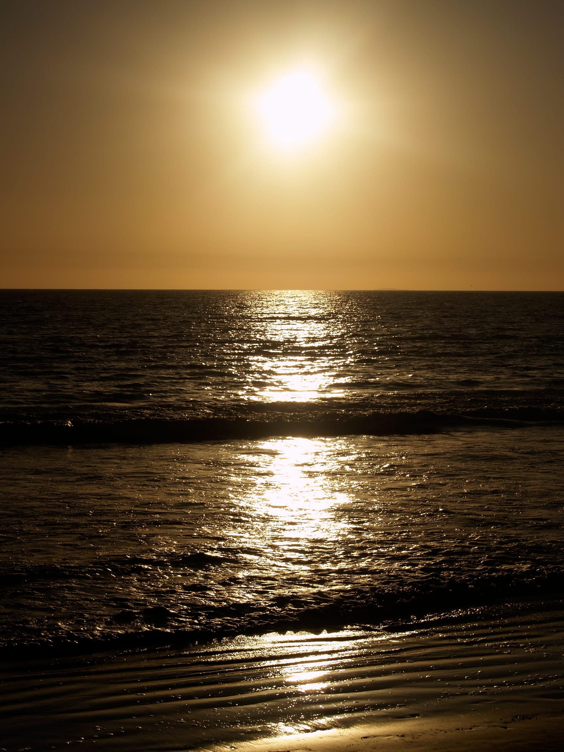 The sun low over the sea, its reflection running up the wet sand.