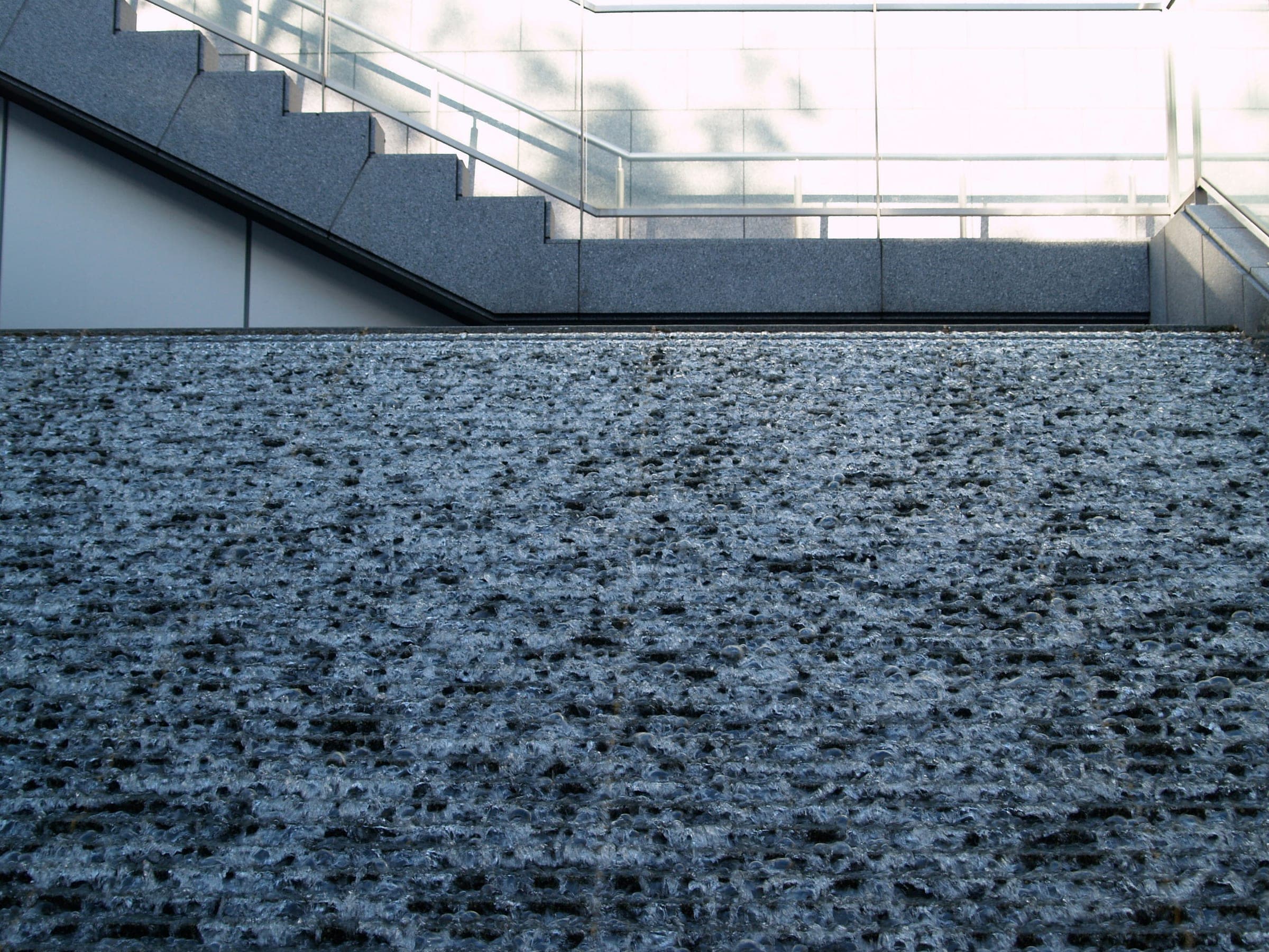Rippling water filling a stone basin below a white stair and railings.