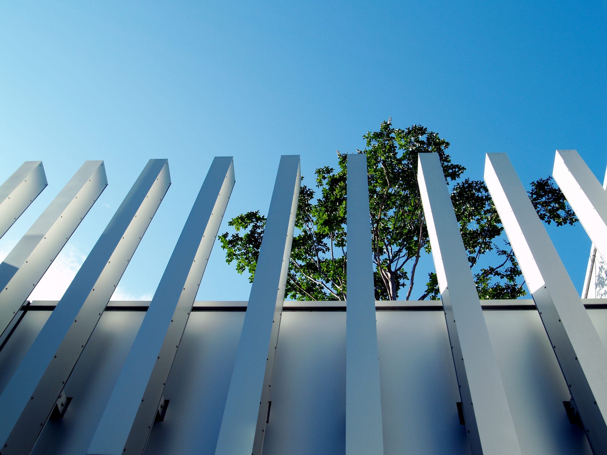 White slatted fins against a blue sky, seen from below, with a tree behind them.