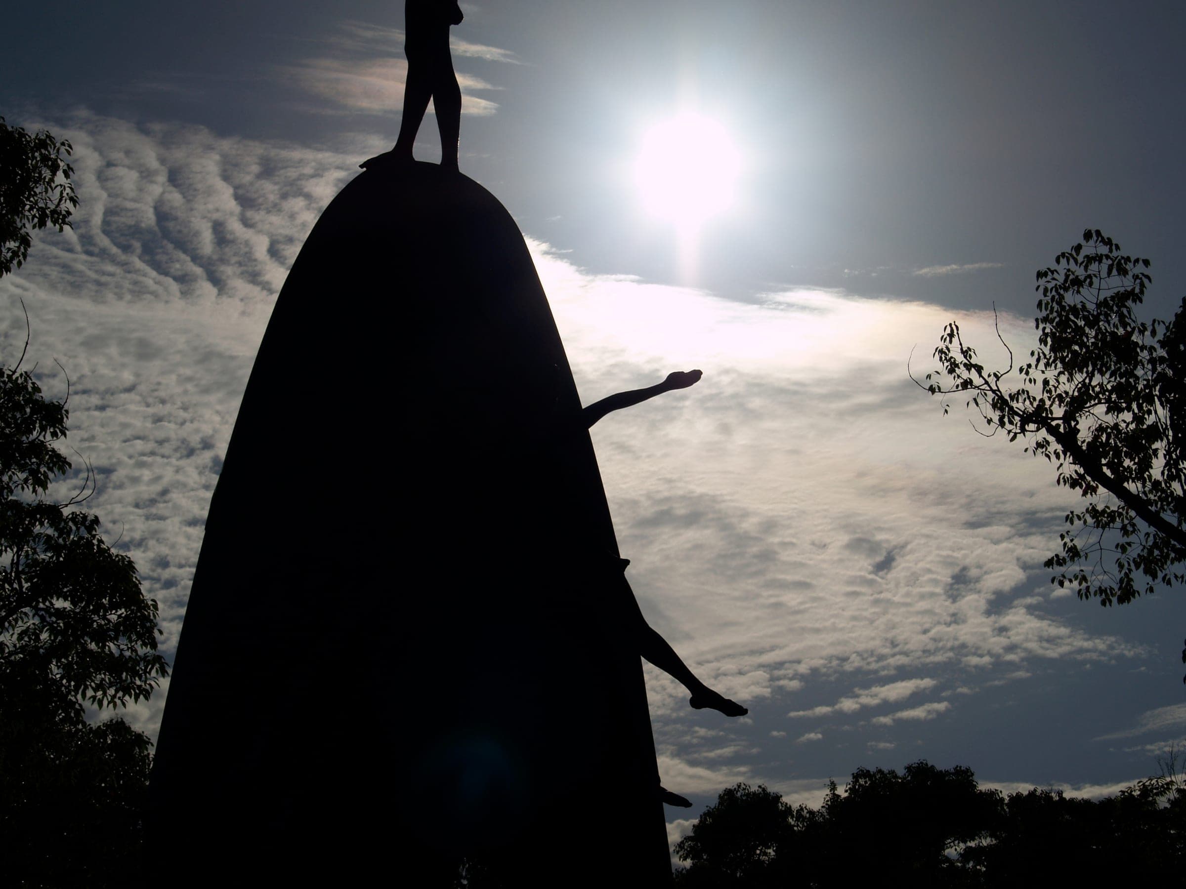 A tall monument topped by a small figure, in silhouette against a bright, hazy sun.