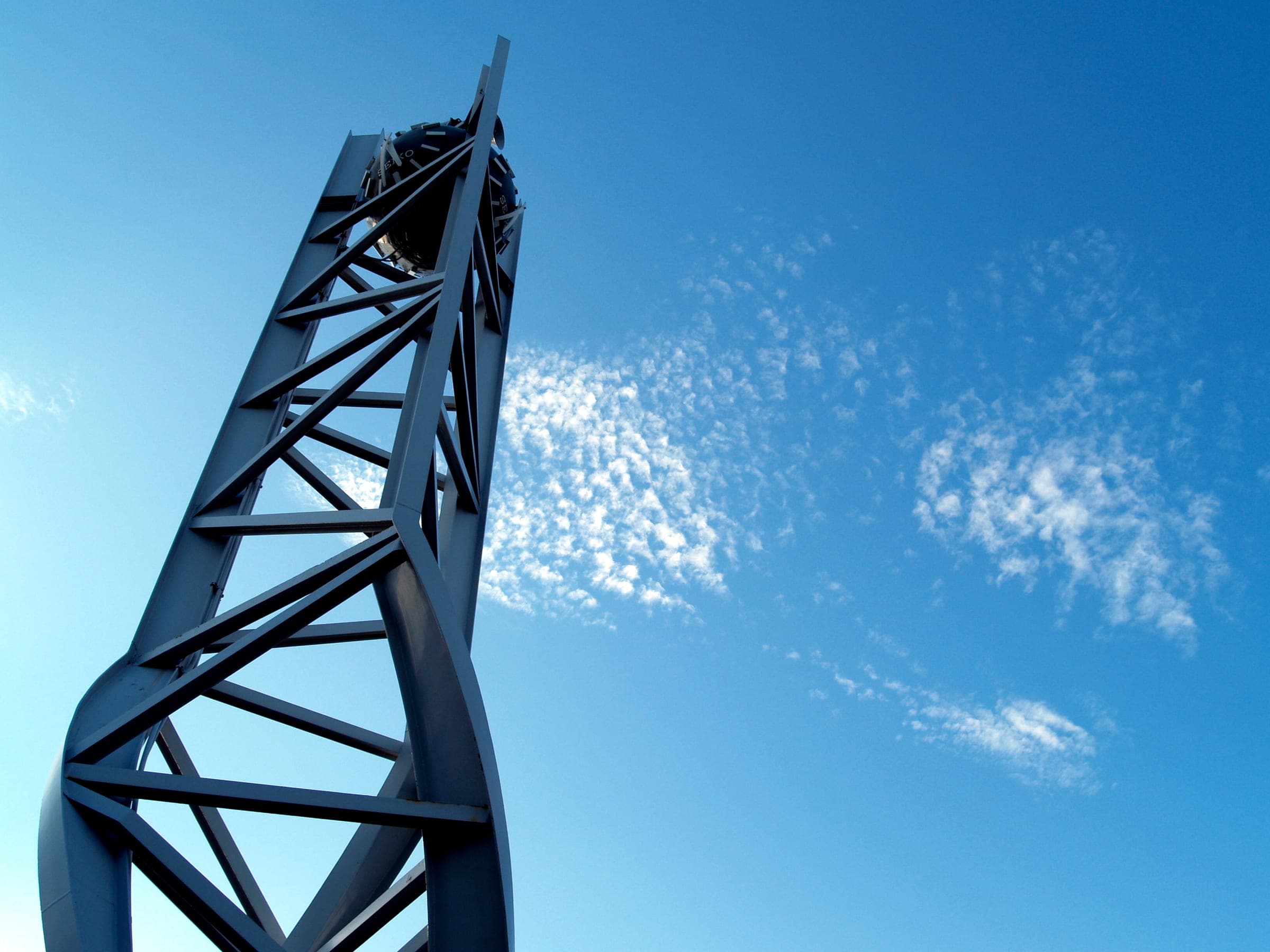 A blue steel lattice structure seen from below against a blue sky with wisps of cloud.