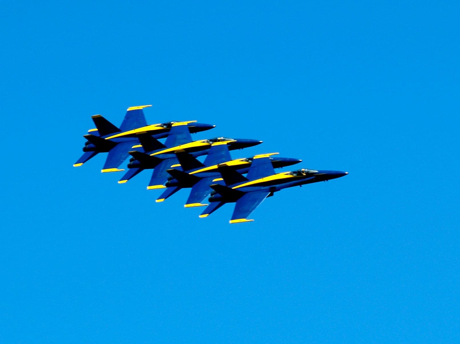 Four jets in tight formation, blue with yellow trim, against a clear blue sky.